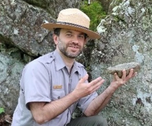 A ranger in a flat hat holds a rock.