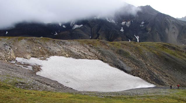 two people walking near a patch of snow on a mountain top