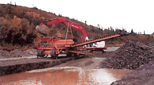 large machine scraping up earth and dumping it into a sluice