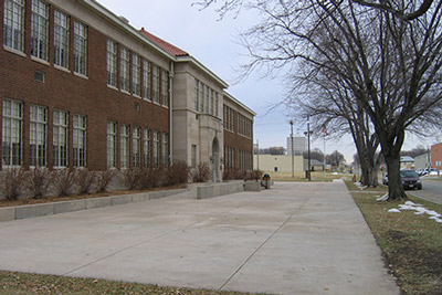 A two-story red brick school opens onto a concrete courtyard.