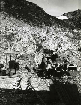 men standing near a rustic railroad track leading into a tiny tunnel in a mountainside
