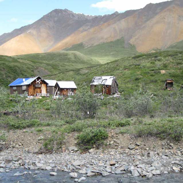 three rustic buildings near a creek with hills and mountains in the distance