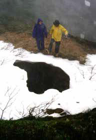 two people standing over a mine opening in the ground