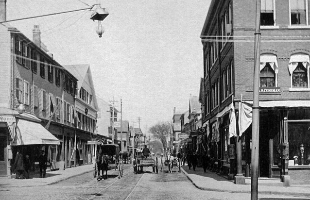 Horse-drawn carts on a cobblestone road with trolley tracks.