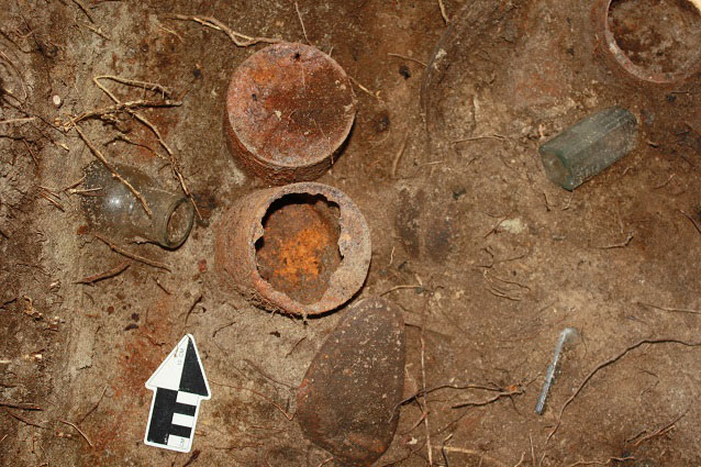 Rusted cans, glass bottles, and shoe soles in dirt with an arrow marking north