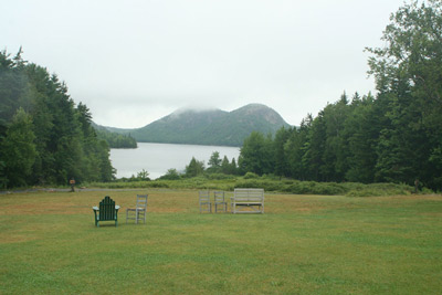 A view of the lawn, tree-encircled Jordan Pond, and surrounding hills.