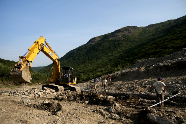 an excavator sits on piles of rocks and gravel