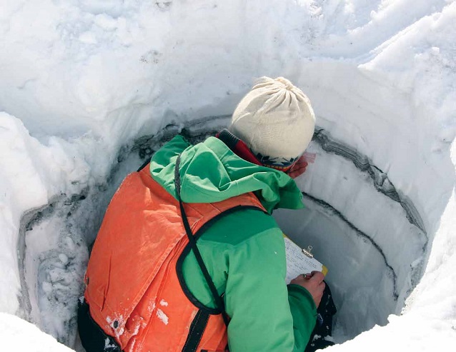 a person sits in in a hole of snow analyzing layers of ash