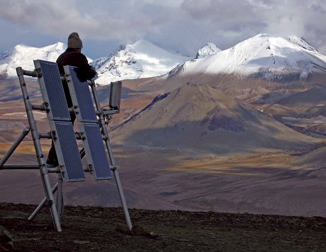 a man stands on solar panels with mountains in the distance