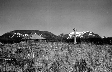 historic photograph of a cross in a field with mountains in the background