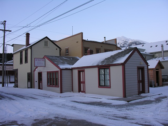 Two small white and red buildings on a snow covered street.