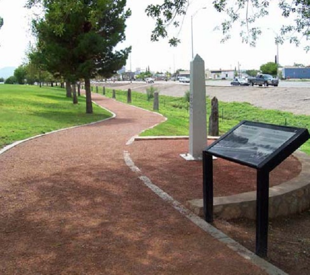 Interpretive wayside and obelisk-shaped monument along a paved trail