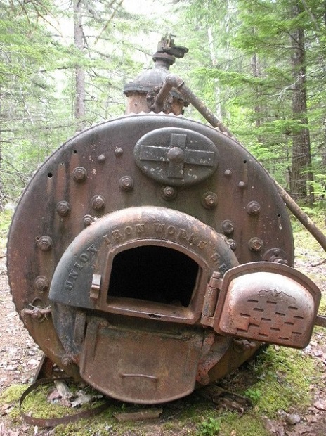 An iron boiler with a door open in a forest.