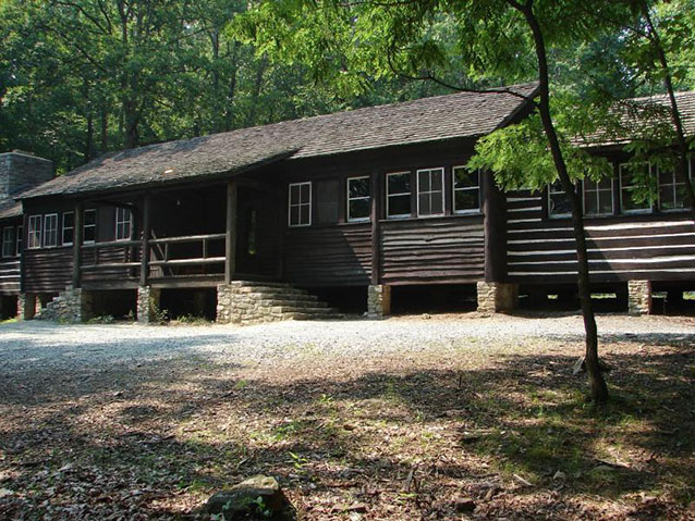 A long, low log building has a porch and stone pillar foundations.