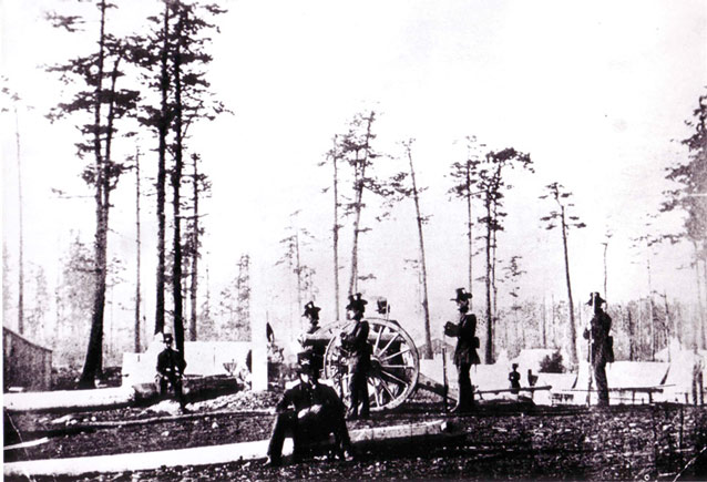 Grainy image of soldiers, a canon, and a scattering of tents in an open forest
