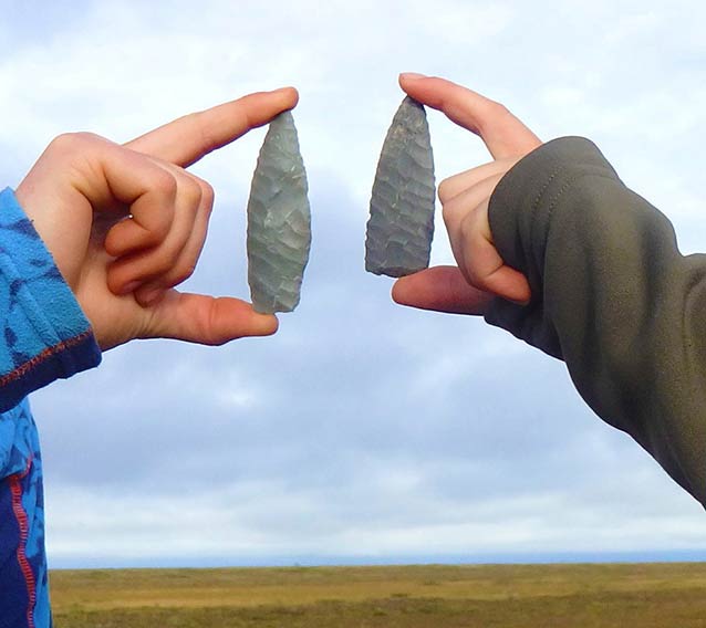 two stone arrow heads, roughly 5 inches long, being held up by two people