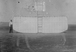 Orville Wright at left wing end of upended glider, bottom view; Kitty Hawk, North Carolina
