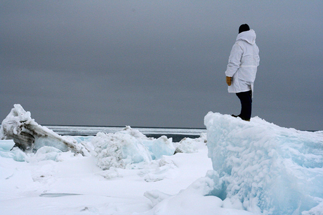 man in a white parka standing on large block of ice looking toward the ocean