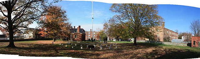 Headstones circle a flagpole in a cemetery in fall, with colorful trees and leaves on the grass.