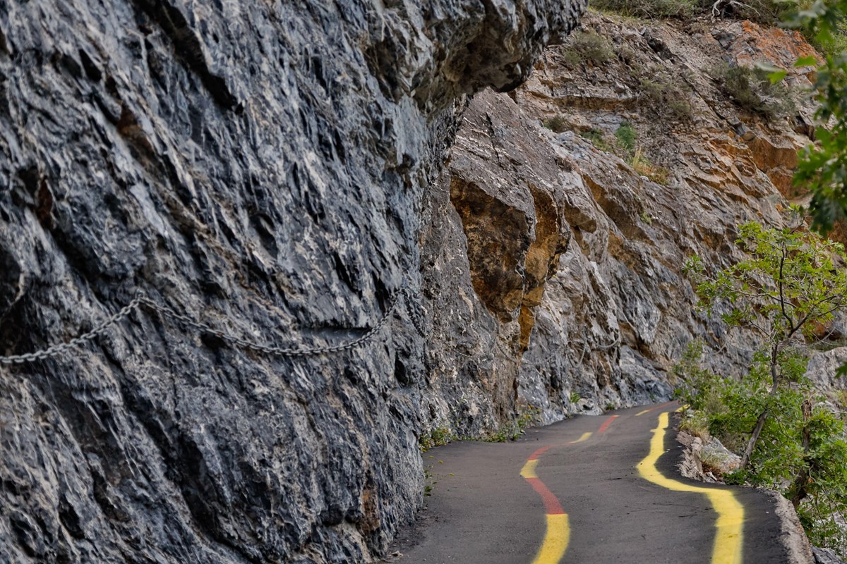 Narrow hiking trail with steep drop offs and red and yellow stripes down the center. 