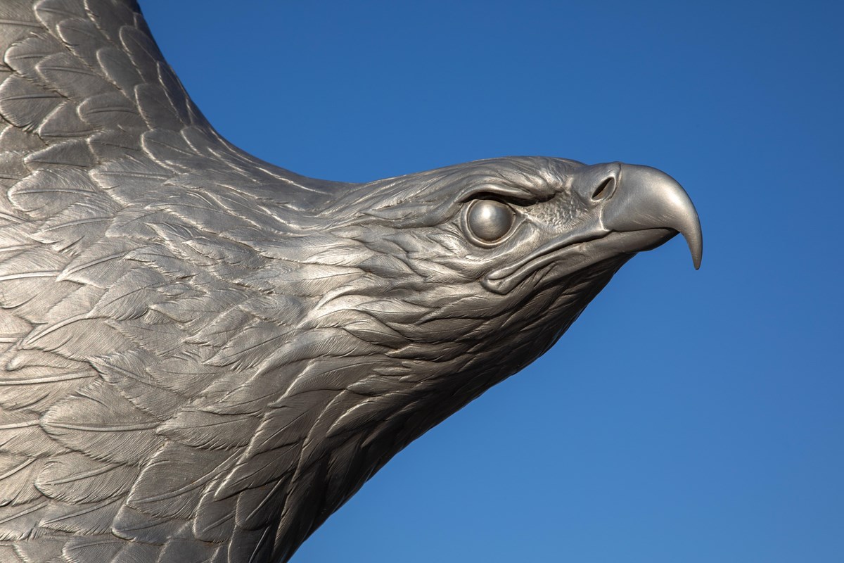A metal sculpture of an eagle in front of a blue sky.