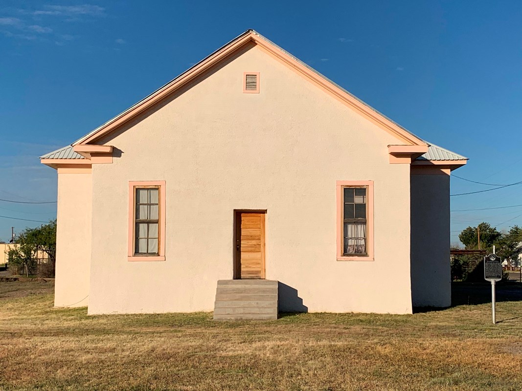 cream colored building with two windows and a wooden doorway with steps leading up to it. 
