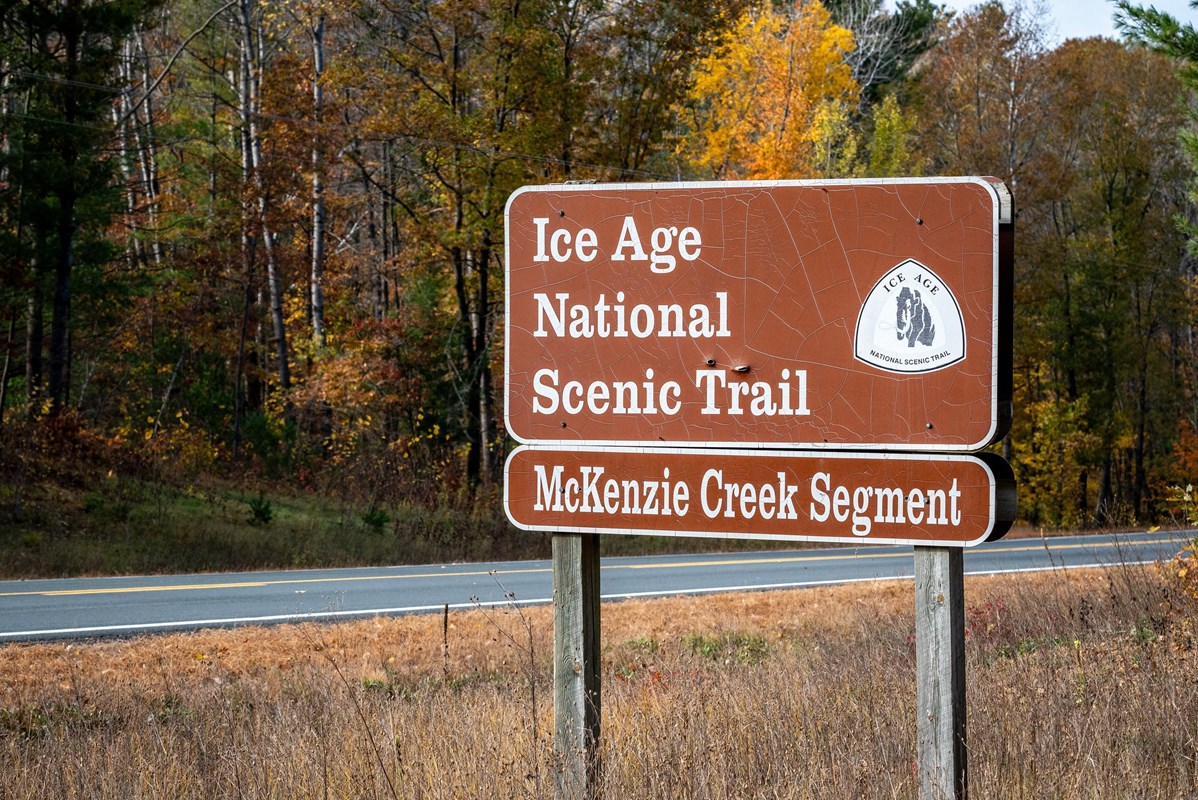 Photograph of &ldquo;Ice Age Trail&rdquo; sign surrounded by a forest with autumn foliage.