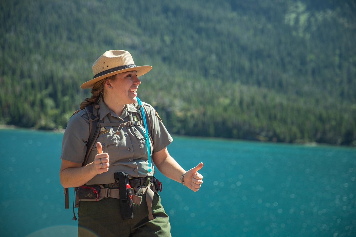 A park ranger gives the thumbs up in front of water. 