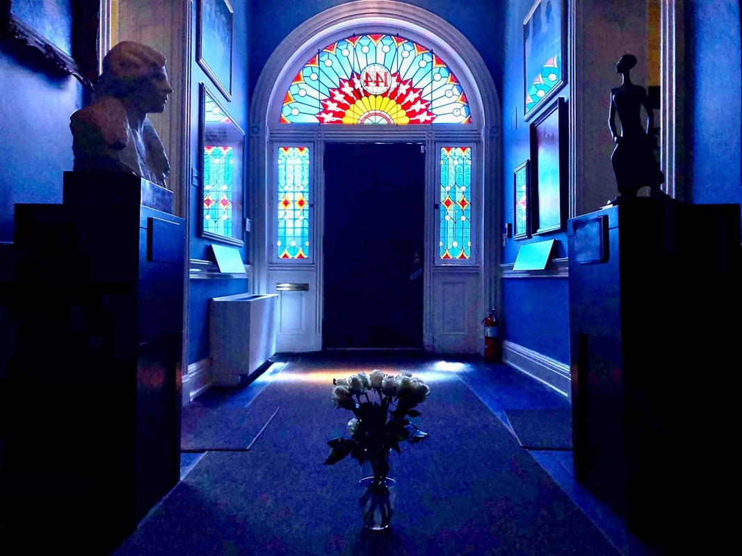 Interior photo of the Hall of Portraits lit by sunlight streaming through stained glass 