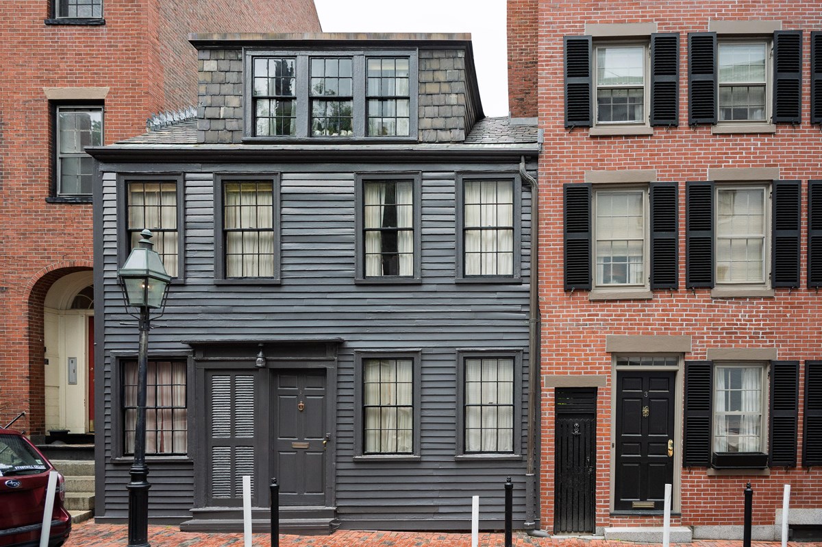 Small gray wood building in between two brick buildings
