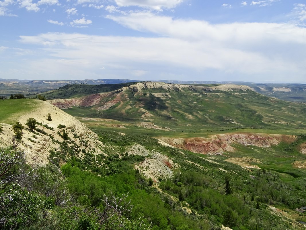 A green valley with a ridgeline across the way with a tan top not covered with vegetation.