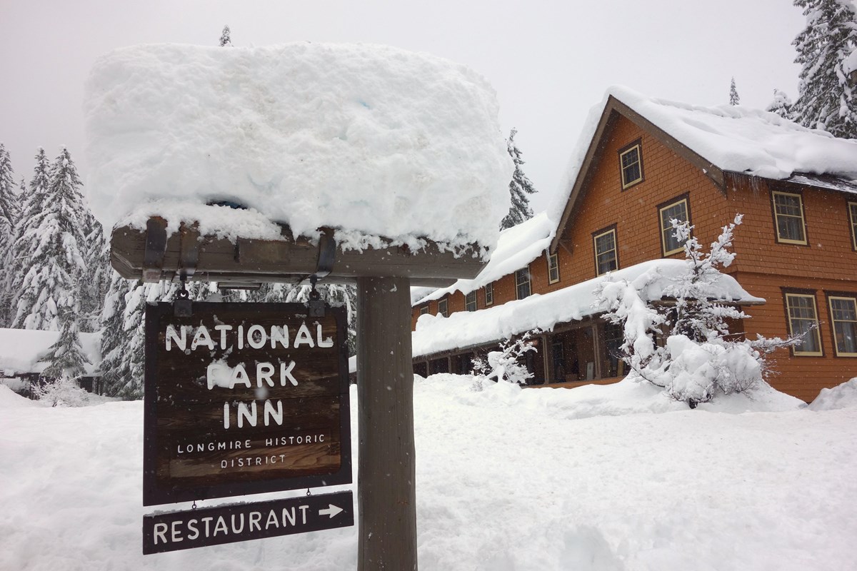A wood "National Park Inn" sign in front of a large wood shingle building covered in deep snow.