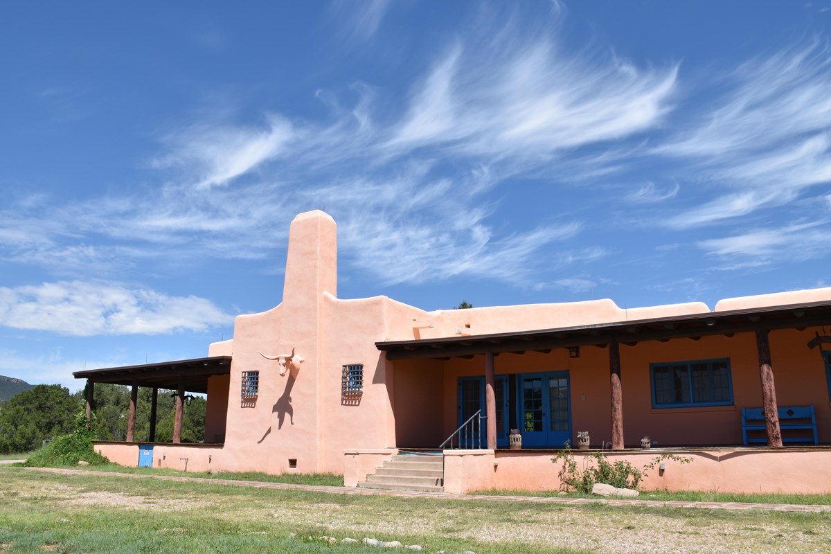 Pink-tan building with chimney and long covered porches at sides, steer head decoration center.