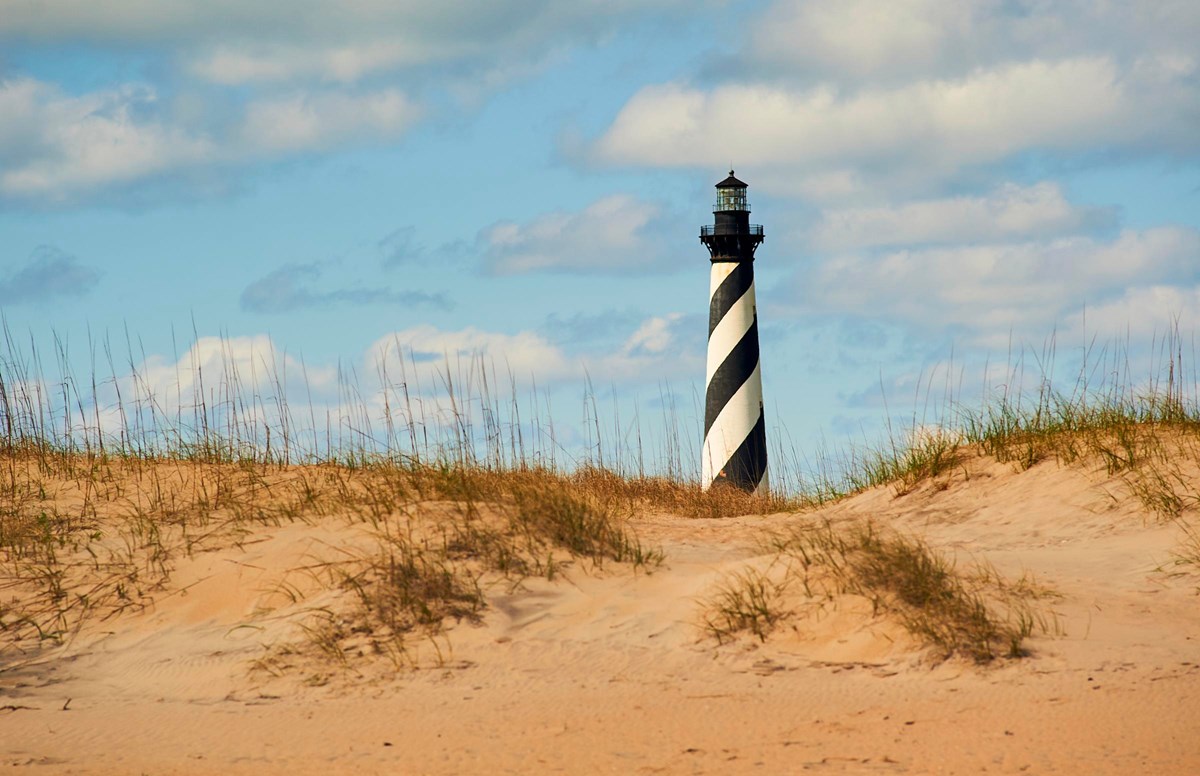 A beach landscape with the black and white spiraled lighthouse in the background