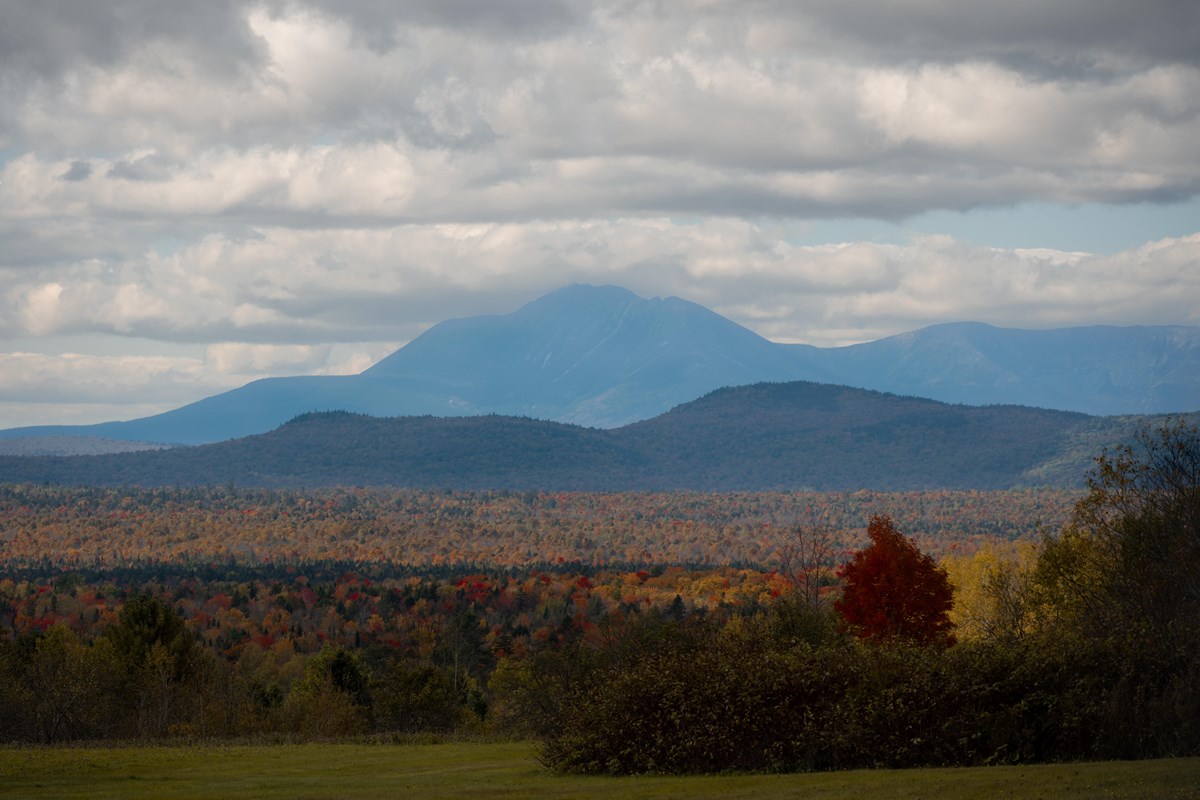 A tall mountain stands behind fall foliage and rolling hills.