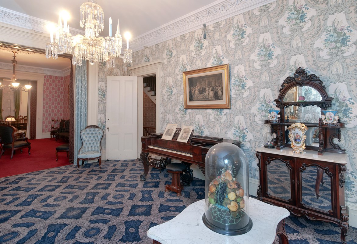 A Victorian-era parlor with blue wallpaper and blue carpeting.