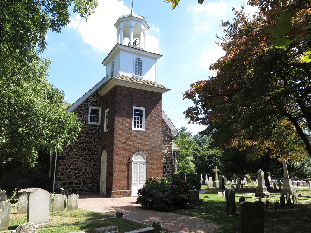 A brick bath leads to a door of an old church surrounded by vegetation. 
