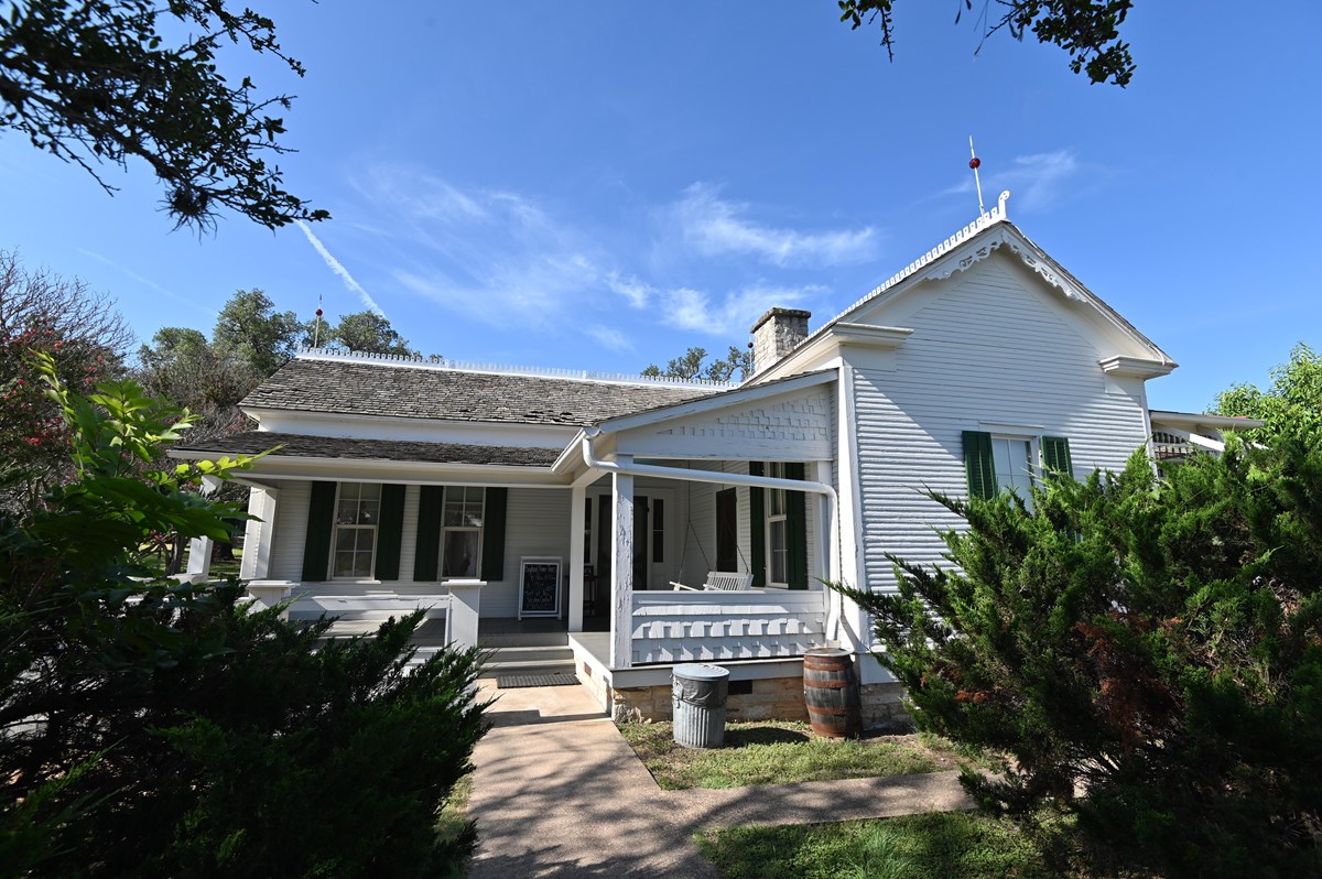 A one-story white frame house with green shutters stands against a brilliant blue sky.