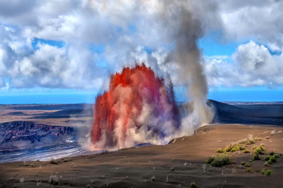 Fountains of molten lava erupting from within a crater next to a whirlwind formed from the eruption.