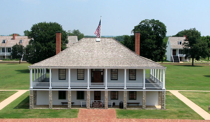 A two-story two-chimney building is surrounded by stone and wooden columns.