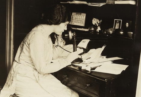 Photograph of Alice Paul, seated at desk, in profile, speaking on telephone
