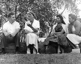 A man and three women sitting on a log outdoors in conversation.