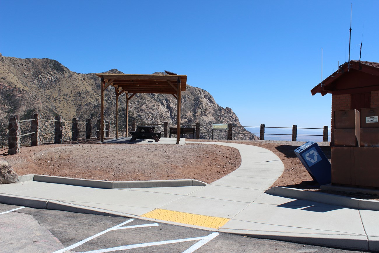 Shade structure with two picnic tables overlooking a valley and mountain peaks.