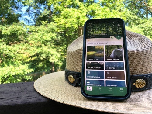 A cell phone leaning on a ranger hat with trees in the background