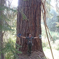 Man with arms out-stretched in front of large Douglas fir tree