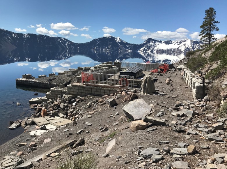 Photos of Cleetwood Marina on a sunny day with calm water causing a mirror reflection of the surrounding mountains. Rockfall is evident around the failed marina bulkhead.