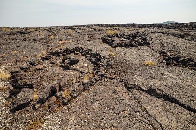 three circles made of black rocks on a lava flow with small piles of rocks in the center of each circle
