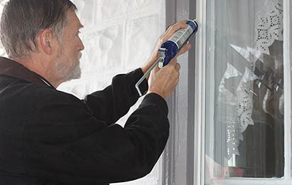 Man using a caulk gun to seal gaps between storm windows and the window frame.