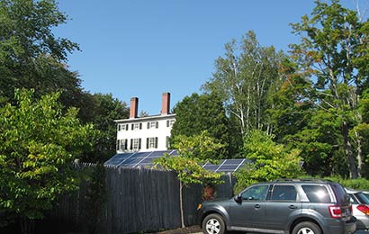 Solar panels supported on poles, with a historic house in the background.
