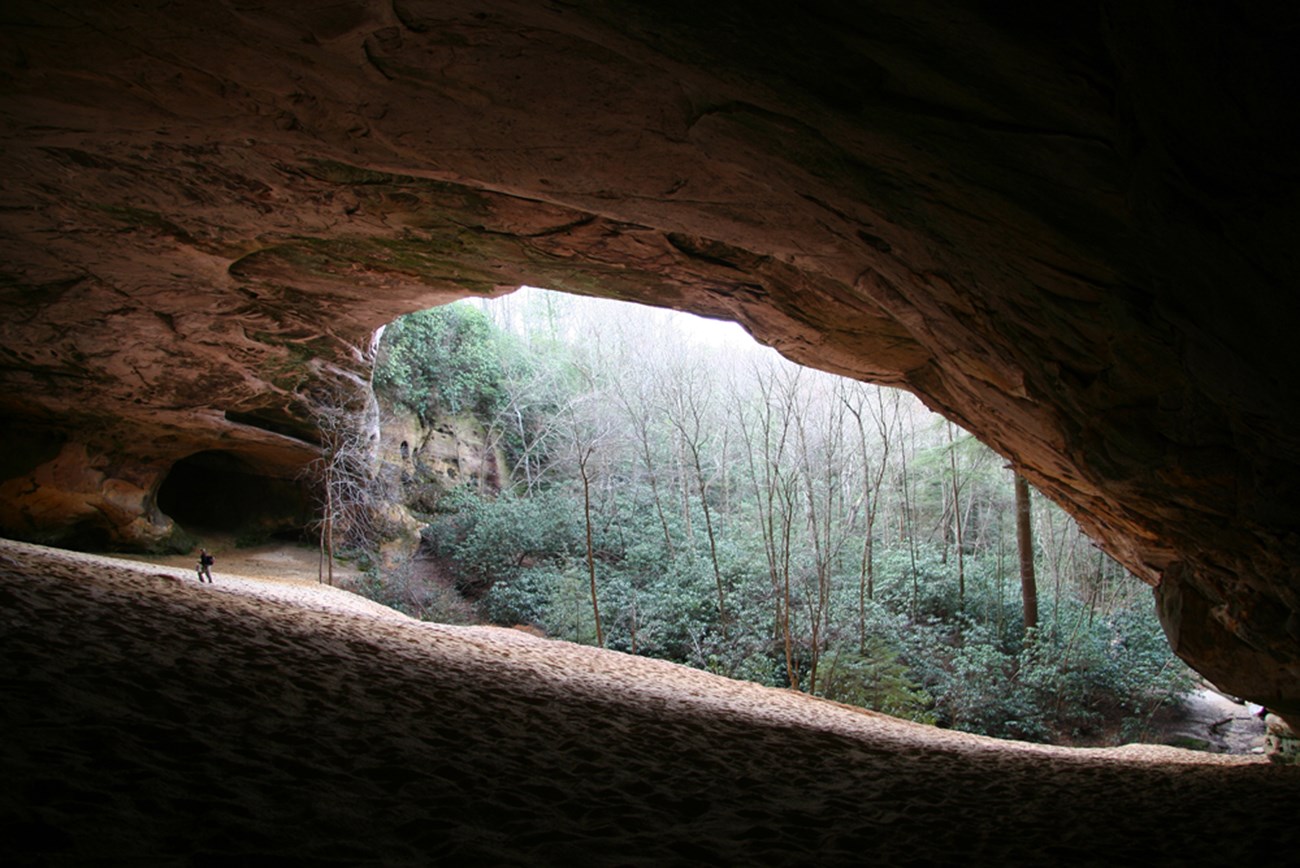 Rock overhang with sand below and a person hiking on the left